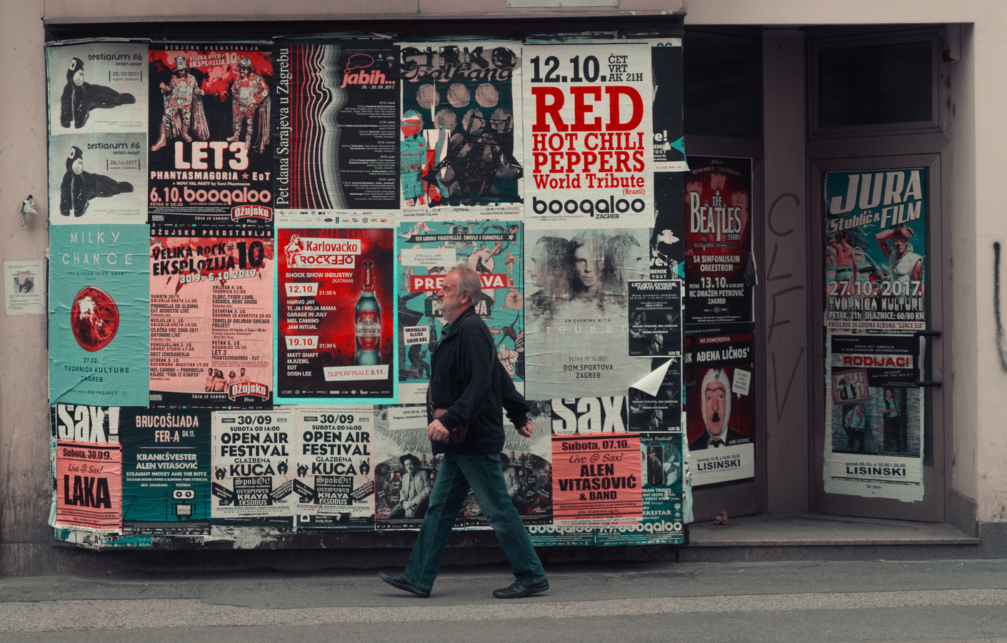 Old man walking near board with posters on street
